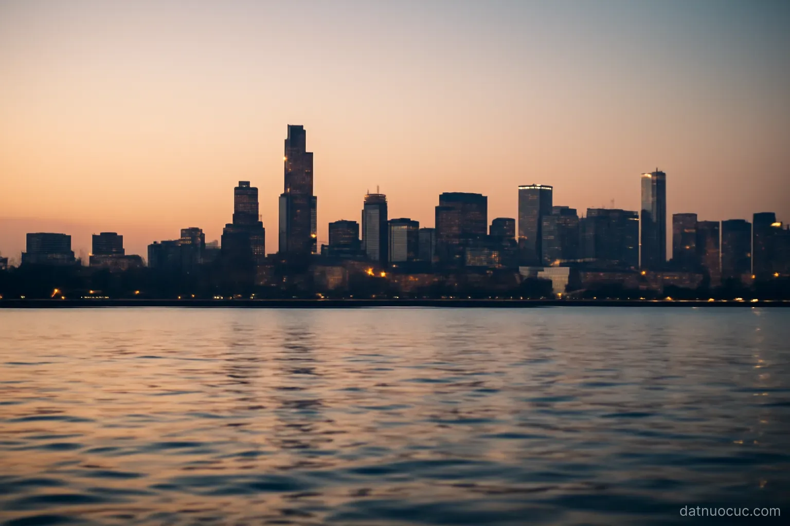 A coastal city skyline seen from across a wide harbour at dusk, calm water in the foreground