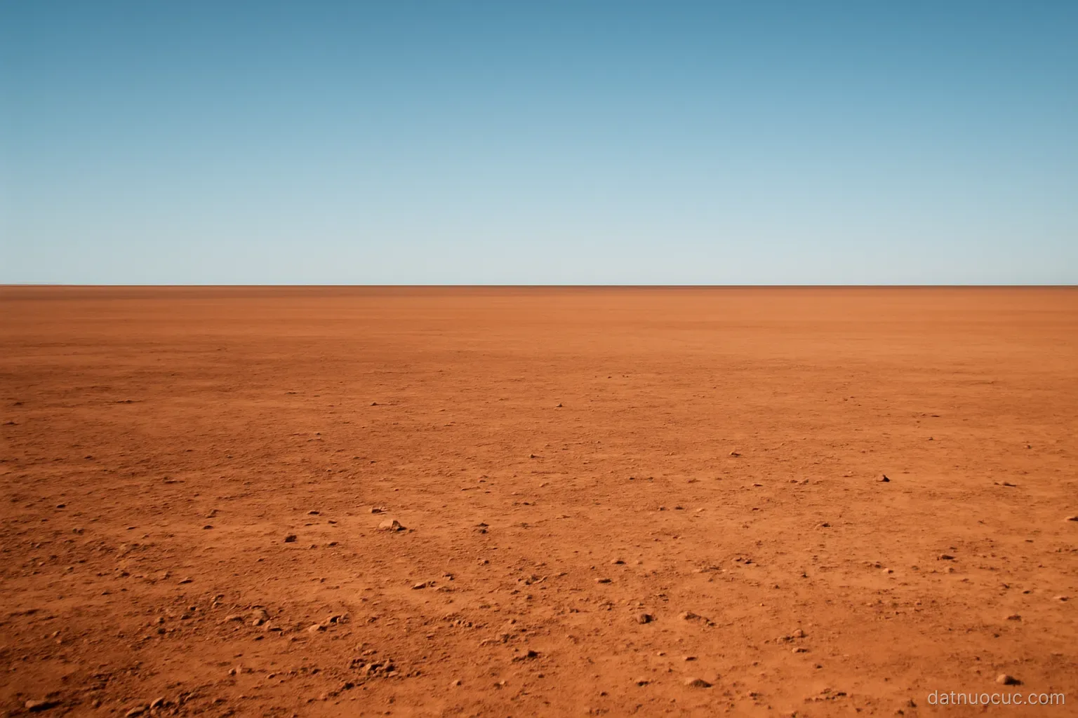 A vast flat red-earth plain stretching to a distant horizon under a wide clear sky, no people or buildings