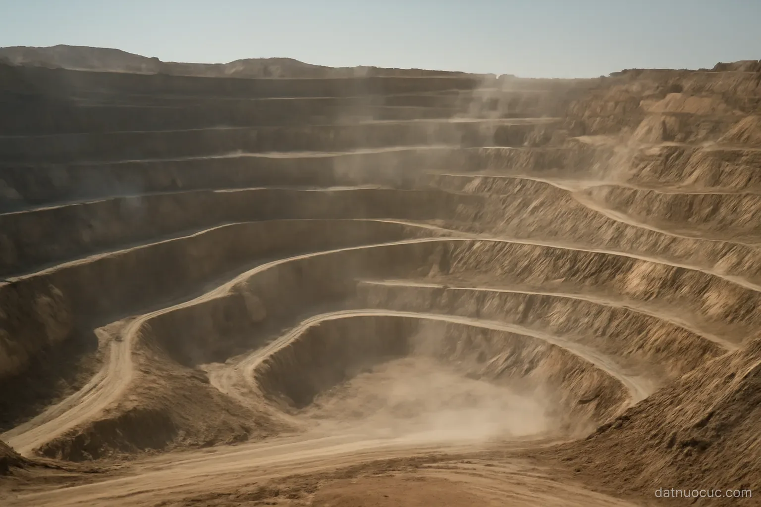 An open-pit mine terrace seen from a distance with haul roads cutting across it, dusty air, no vehicles